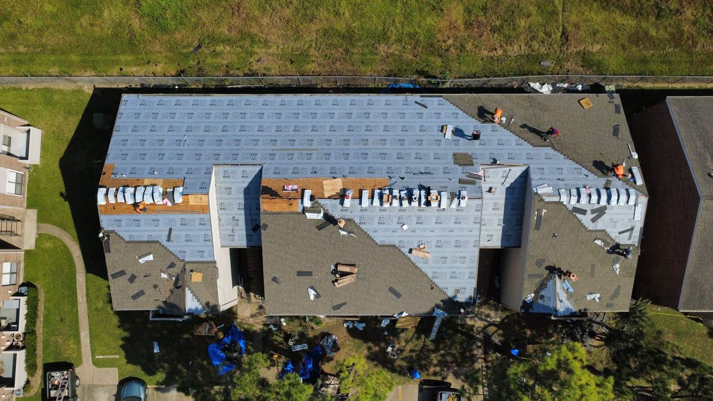 Multifamily re-roof in progress: full tear-off, synthetic underlayment dried in, shingle bundles staged by section
